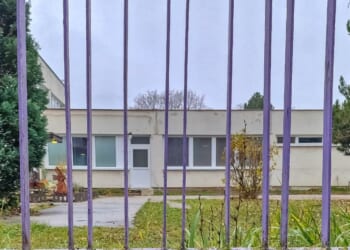 An empty school building behind a purple metal gate on a cloudy autumn day.