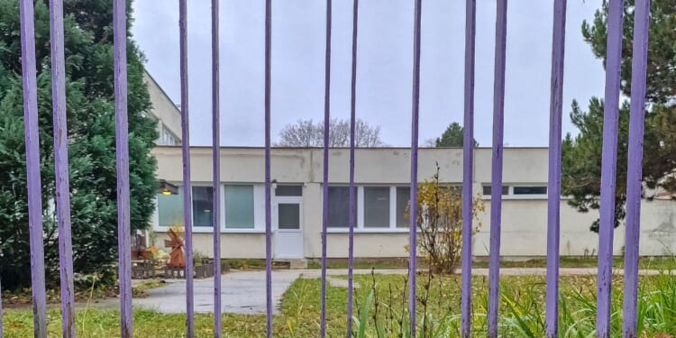 An empty school building behind a purple metal gate on a cloudy autumn day.