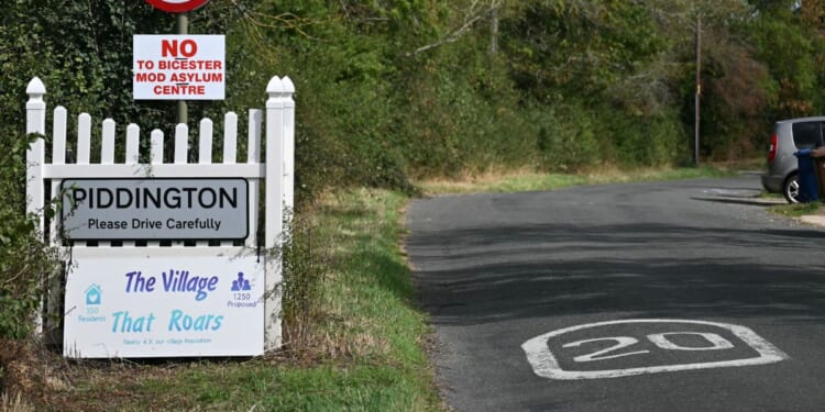 A sign for the village of Piddington, England, is pictured next to another saying 'No to Bicester MOD asylum centre,' in reference to a government plan to house some 1,200 male asylum seekers nearby.