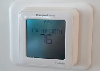 Pictured in a white room a Honeywell thermostat can be seen on a wall at 76 degrees.