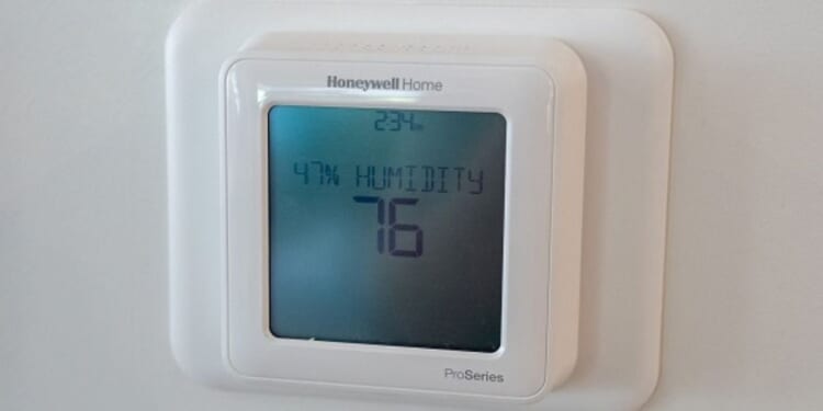 Pictured in a white room a Honeywell thermostat can be seen on a wall at 76 degrees.