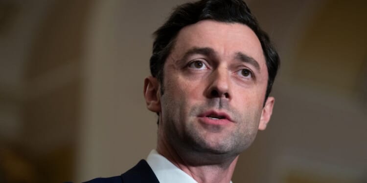 Senator Jon Ossoff is pictured in a suit and speaks, looking slightly to the side, with a neutral background and soft lighting focused on his face.