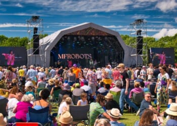 A large crowd in front of a stage at an outdoor summer music festival in England.