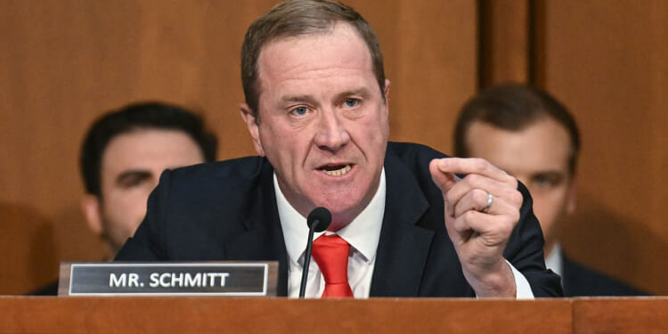 Sen. Eric Schmitt filed a parental rights bill declaring that failure to "affirm" a transgender identity is not abuse. Pictured: a man in a suit and red tie speaks emphatically at a hearing or meeting, gesturing with his hand. A nameplate reading MR. SCHMITT is on the desk in front of him. Other people are seated in the background.