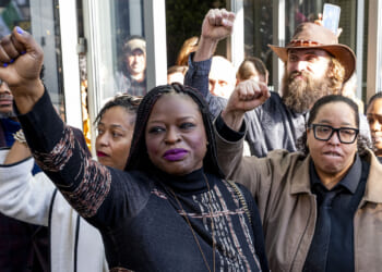 Nekima Levy Armstrong and others who invaded Cities Church. A group of people stand together with raised fists, showing solidarity. The central figure, a woman in a patterned top, looks determined. Others around her also have fists raised and appear resolute.