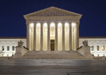 The Trump administration asked the Supreme Court to allow the Bureau of Prisons to cease providing sex-rejecting procedures, citing a memo about the unreliability of the World Professional Association for Transgender Health or WPATH. Pictured: The U.S. Supreme Court building at night, its columns and steps illuminated by bright lights, with statues on either side of the entrance and a dark blue sky in the background.