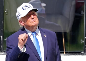 Donald Trump in a hat stands outdoors, raising his fist and smiling.