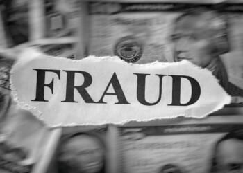 A torn piece of paper with the word FRAUD is placed over blurred U.S. dollar bills, suggesting financial deception or crime.
