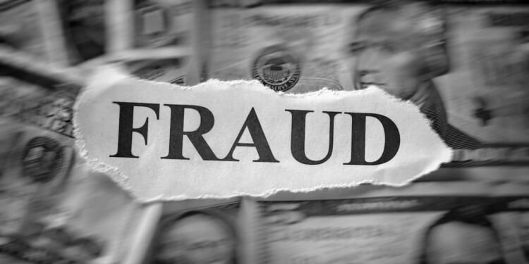 A torn piece of paper with the word FRAUD is placed over blurred U.S. dollar bills, suggesting financial deception or crime.
