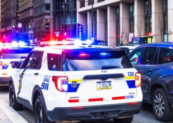 Police vehicles with their lights flashing alongside traffic in downtown Philadelphia.