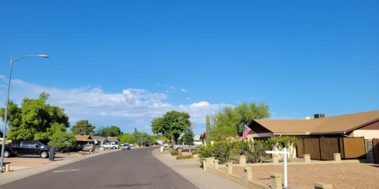 A residential street in Phoenix, Arizona, showcases single-story ranch homes and classic southwestern desert xeriscape landscaping.