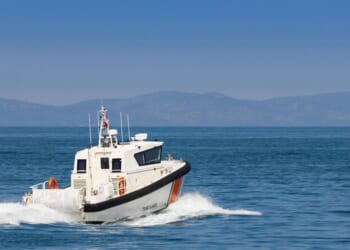 The rear view of a white Coast Guard patrol boat cruising at high speed on blue sea water.