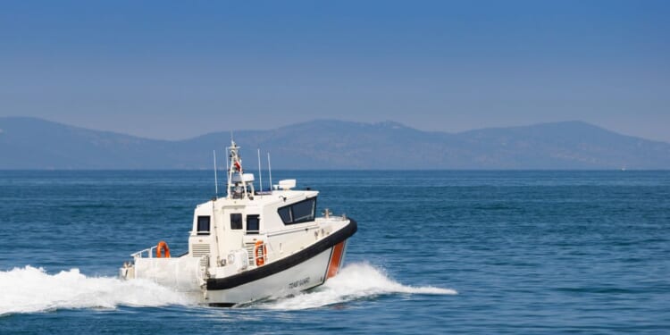 The rear view of a white Coast Guard patrol boat cruising at high speed on blue sea water.