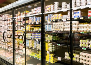 Fridges in a grocery store aisle are illuminated by light.