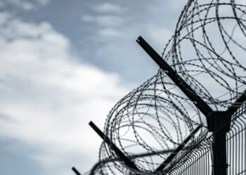 A prison fence with razor wire against a dark sky.