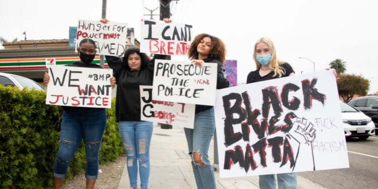Young women wear protective masks and hold signs in support of Black Lives Matter on May 28, 2020, in Marina del Rey, California.