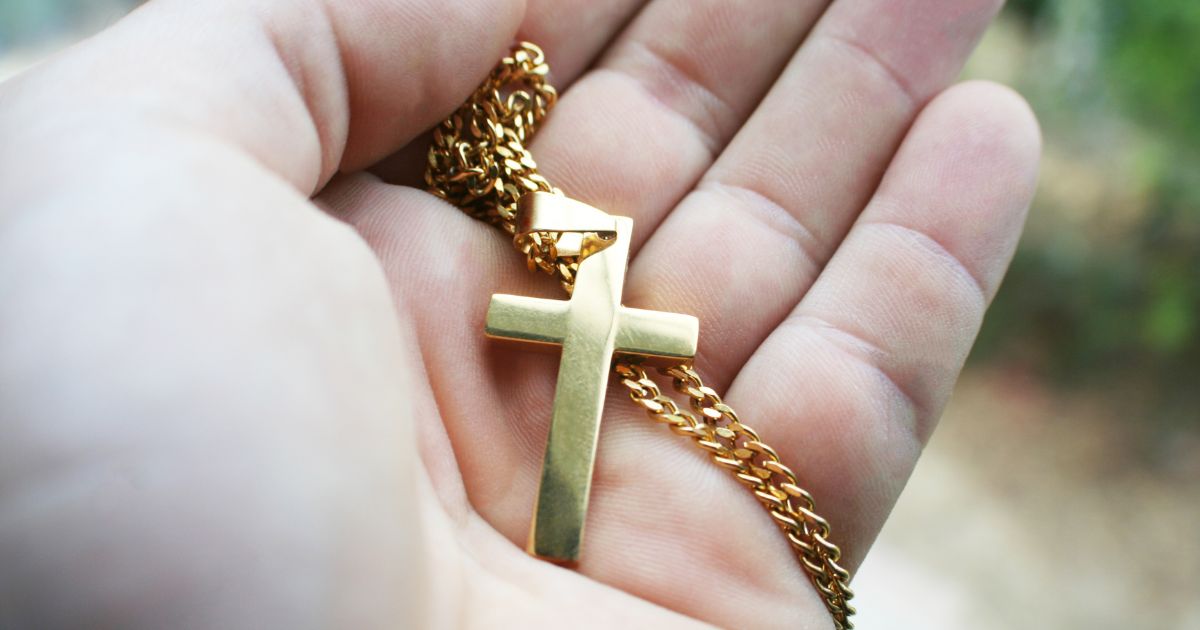 A gold cross in the palm of a hand.
