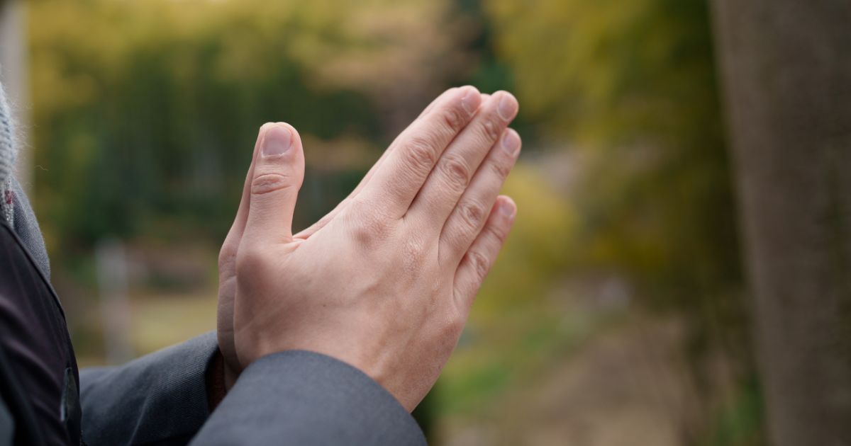 A man clasping his hands together to pray.