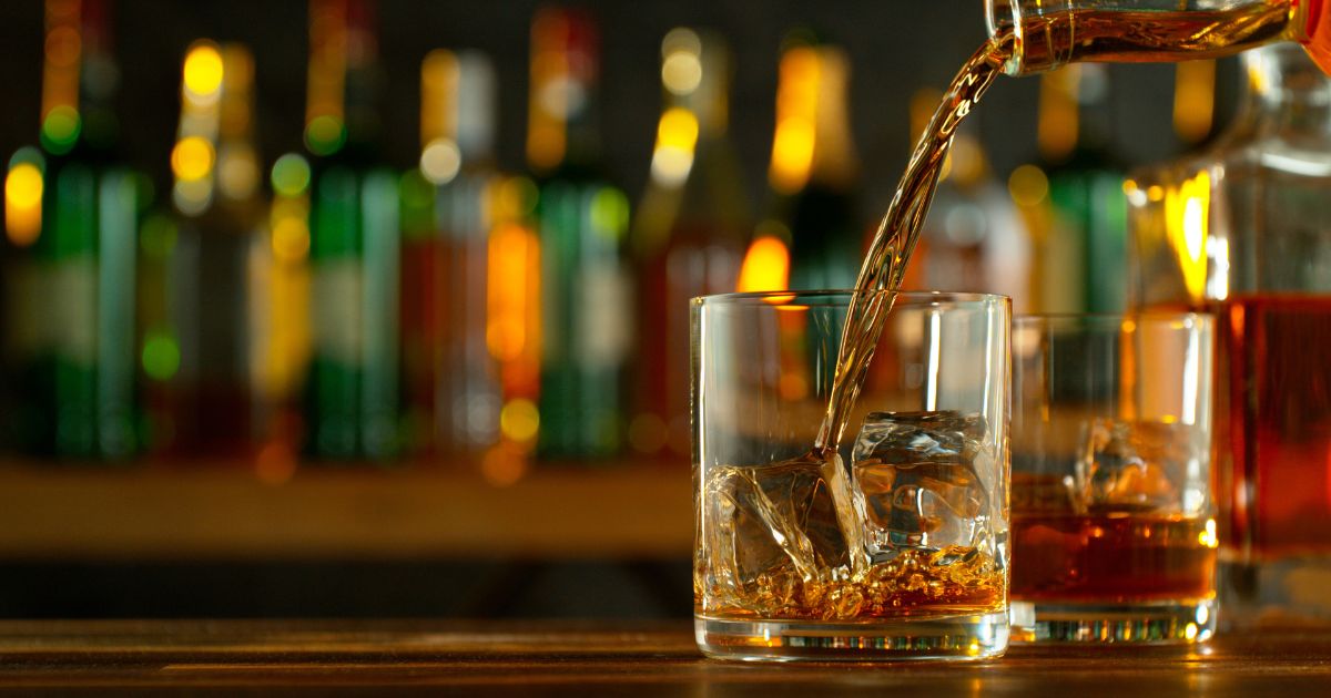 A glass of whiskey or rum on a bar as it is poured.