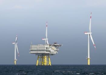 The photo presents a wide, horizontal view of the Borkum Riffgrund wind farm, where several wind turbines are erected in the open sea.