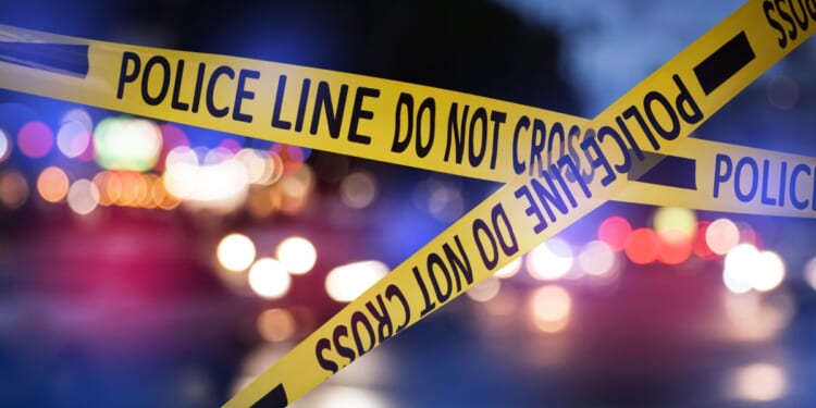 This Getty stock image shows police tape in the foreground of a crime scene at night.