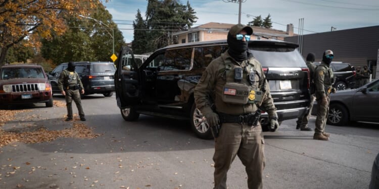 Federal agents stand guard as they are confronted by residents after making a stop while driving in a caravan through the Brighton Park neighborhood on Nov. 6, 2025, in Chicago, Illinois.