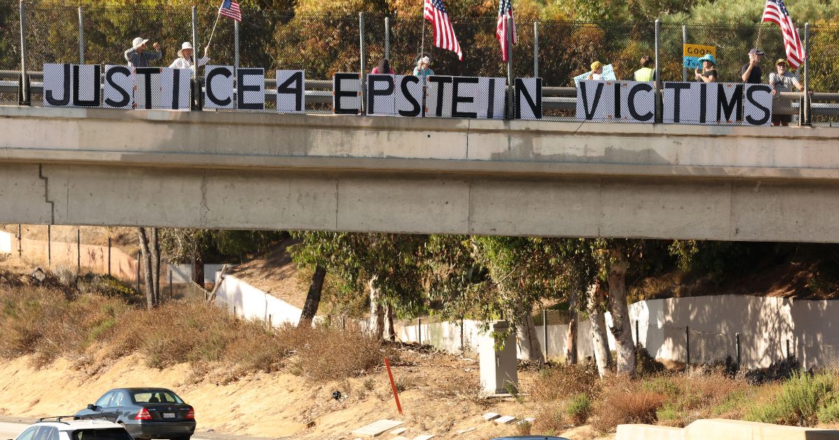 People hold American flags and signs reading "Justice 4 Epstein Victims" on a freeway overpass in Encinitas, California, on July 31, 2025.