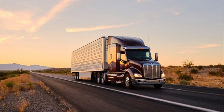 A large semi truck hauls freight down an open highway in the Western United States.
