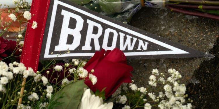 A Brown University pennant is covered by flowers left by mourners at a makeshift memorial on the campus of Brown University, in Providence, Rhode Island, after a mass shooting Saturday that left two people dead and nine others wounded.