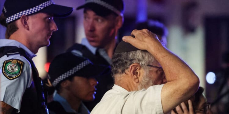 A member of the Jewish community reacts next to Australian law enforcement officers at the scene of the Bondi Beach shooting in Sydney on Dec. 14, 2025.