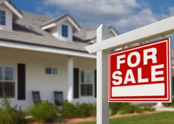 A "For Sale" sign sits on a house's front lawn.