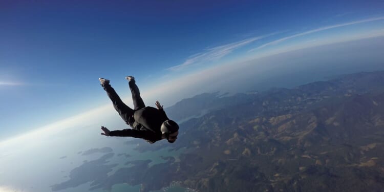 A skydiver jumps over the sea and mountains.