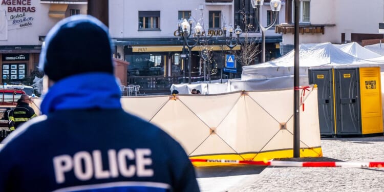 A police officer patrols on front of folding screens set up around the Constellation bar in the luxury Alpine ski resort town of Crans-Montana, on January 1, 2026 after a fire ripped through the venue during the New Year's Eve celebrations. Several dozen people are presumed dead and around 100 injured after a fire ripped through a crowded bar in the luxury Swiss ski resort of Crans-Montana, Swiss police said.