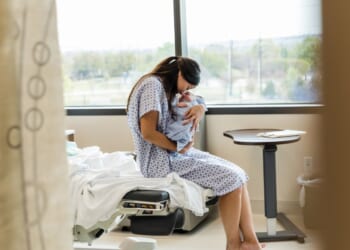 A Chinese mother lovingly holds her newborn baby in a hospital room.