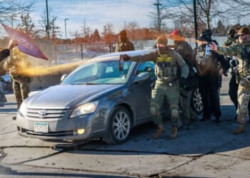 Federal agents use pepper spray against a protester holding a sign during an enforcement operation outside the Whipple Building, an ICE facility in Minneapolis, Minnesota, on Jan. 11, 2026.