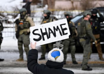 An onlooker holds a sign that reads "Shame" as members of law enforcement work the scene following a suspected shooting by an ICE agent during federal law enforcement operations on Jan. 7, 2026, in Minneapolis, Minnesota.