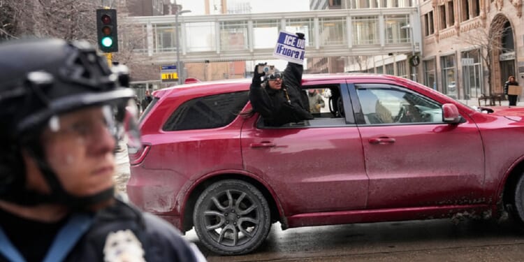 A protester holds a sign reading, "ICE Out," out of a car in Minneapolis on Saturday.
