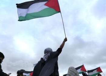 A protester waves a Palestinian flag while another holds a banner saying "Shut Elbit Down" during the demonstration on Jan. 23, 2026, in Sandwich, United Kingdom.
