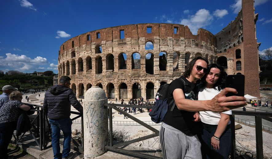 A couple take a selfie photo in front of the new outdoor space created with travertine marble around the Colosseum, during it's inauguration in Rome, Tuesday, March 17, 2026. (AP Photo/Andrew Medichini)