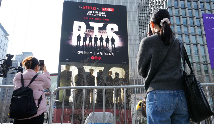 People take photos of a screen promoting a comeback concert of K-pop group BTS at Gwanghwamun Square in Seoul, Wednesday, March 18, 2026. (AP Photo/Ahn Young-joon)