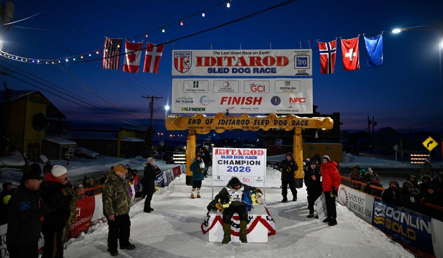 Jessie Holmes poses with his lead dogs Zeus, left, and Polar, after claiming his second straight Iditarod Trail Sled Dog Race championship, in Nome, Alaska, Tuesday March 17, 2026. (Marc Lester/Anchorage Daily News via AP)