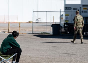 An Afghan refugee sits and watches as U.S. military service members pass in an Afghan refugee camp on Nov. 4, 2021, in Holloman Air Force Base, New Mexico.
