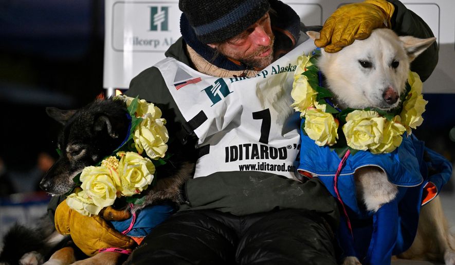 Jessie Holmes poses with his lead dogs Zeus, left, and Polar, after claiming his second straight Iditarod Trail Sled Dog Race championship, in Nome, Alaska, Tuesday March 17, 2026. (Marc Lester/Anchorage Daily News via AP)