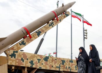 A ballistic missile launch vehicle sits as two women walk past in Tehran on Feb. 11, 2026.