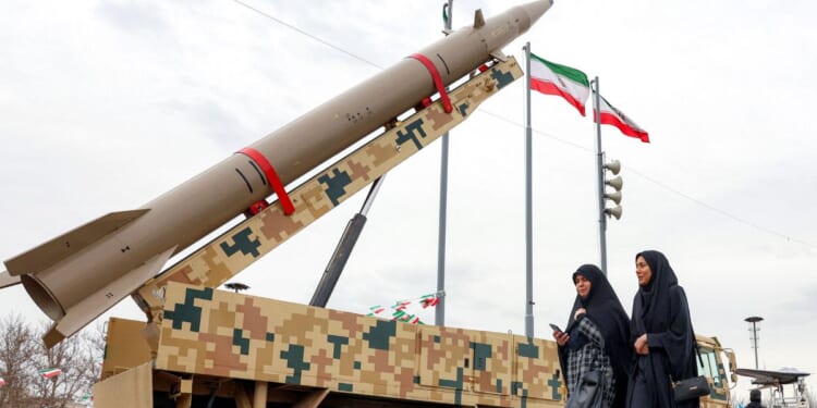 A ballistic missile launch vehicle sits as two women walk past in Tehran on Feb. 11, 2026.