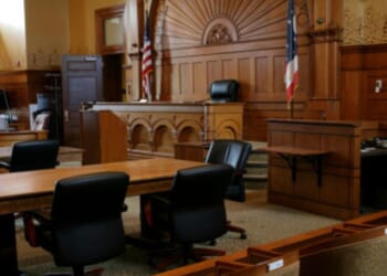 An empty, brown-paneled courtroom with flags.