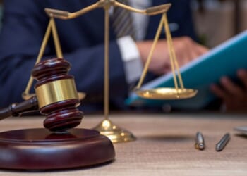 A person sits at a desk analyzing files as the weights of Justice stand and a gavel sits.