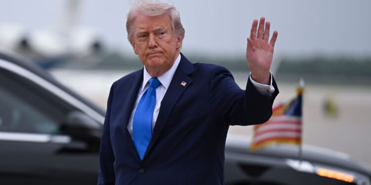 President Donald Trump waves to reporters at an airport.