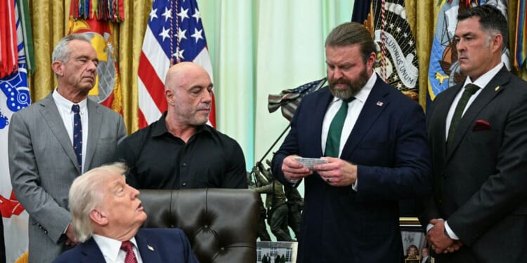 Health and Human Services Secretary Robert F. Kennedy Jr., President Donald Trump, and media personality Joe Rogan listen as W. Bryan Hubbard, CEO of Americans for Ibogaine, speaks before Trump signs an executive order in the Oval Office of the White House in Washington, D.C., on April 18, 2026.