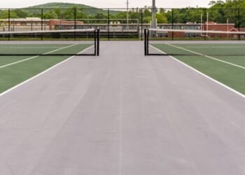 A new green tennis court with white lines and gray outside of the play area.